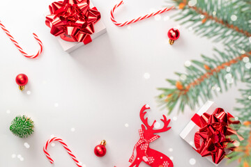 Holiday winter red. White gift box with scarlet ribbon, New Year balls, candy and winter tree in Christmas composition on white background for greeting card. Festive decoration, copy space.