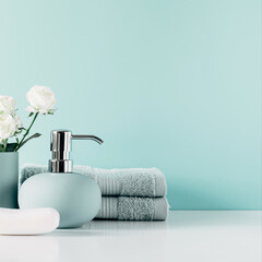 Soft light bathroom decor in mint color, towel, soap dispenser, white roses flowers, accessories on pastel mint background. Elegant decor bathroom interior