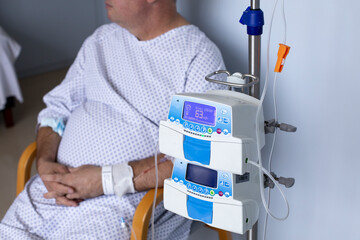 Overweight man sitting in a chair with a dropper, equipment in the foreground, patient in hospital