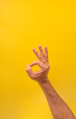 Man's hand making ok gesture on yellow background with copy space