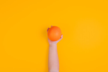 Little girl hand with orange fruit on orange background. Top view. Copy space