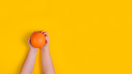 Hands of little girl with orange fruit on orange background. Top view. Banner. Copy space