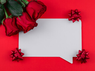 White sheet, three roses ribbon on a red background with place for text in the middle, top view close-up.