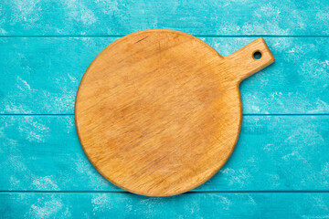Round wooden cutting board for pizza on blue wooden table. Mockup for food project. Top view
