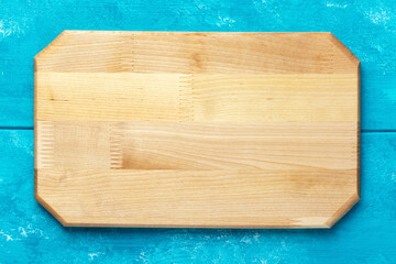 New rectangular wooden cutting board on blue wooden table. Mockup for food project. Top view