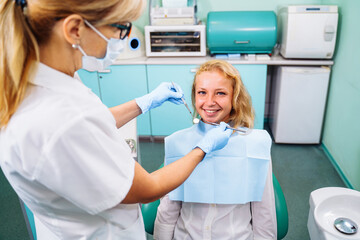 Beautiful young girl at the dentist appointment. An experienced dentist checking the health of patients teeth in a modern dental office. Portrait of smiling girl on a dental chair in dentistry