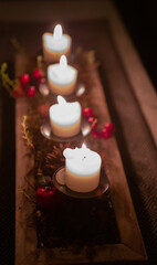 Four burning candles on a dark background with red berries, moss, succulent and pine cone