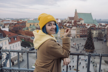 Happy young woman portrait with colored blue hair in coat in front of old town and Christmas tree
