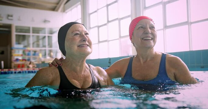 Two senior women embracing together in swimming indoor pool