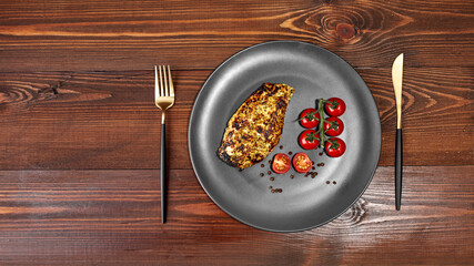 fried chicken fillet on a plate with cherry tomatoes, on a wooden texture next to a fork and knife. Top view with a copy of the text layout space