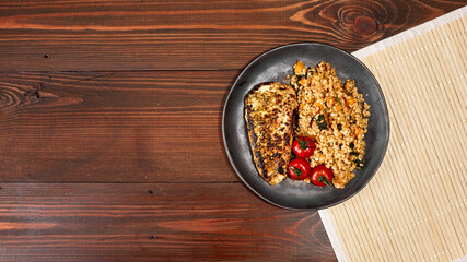 Bulgur with chicken fillet and cherry tomatoes on a plate on a wooden table. Top view with copy space