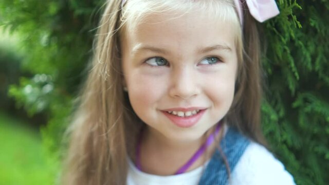 Portrait of pretty child girl standing outdoors in summer park smiling happily.