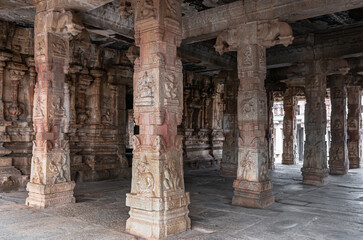 Fototapeta premium Hampi, Karnataka, India - November 5, 2013: Sri Krishna temple in ruins. Brown reddish sculpted pillars supporting mandapam in front of sanctum.