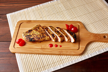 slices of fried chicken fillet on a cutting board with tomato slices on a bamboo mat with copy space to decorate the text