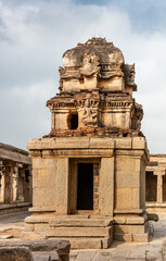 Hampi, Karnataka, India - November 5, 2013: Sri Krishna temple in ruins. Brown stone damaged small shrine with molded vimanam partly restored with red bricks under blue cloudscape.