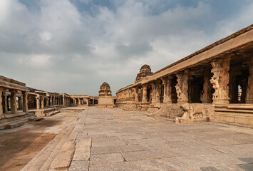 Fototapeta premium Hampi, Karnataka, India - November 5, 2013: Sri Krishna temple in ruins. View along the main building, the Mandapa,m and inner sanctum, all in shades of brown stone under blue cloudscape.