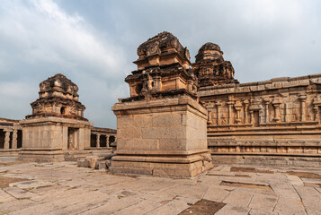 Hampi, Karnataka, India - November 5, 2013: Sri Krishna temple in ruins. 2  brown small shrines in front of main temple building, all with darker brown vimanams on top under light blue cloudscape.