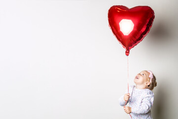 Little girl catches a heart air balloon on a light background. Concept for Valentine's Day,...