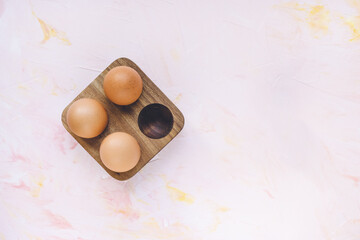 Three brown eggs in a wooden storage organizer box on pink background. Useful household items, organic healthy bio product and Easter holiday concept. Top view, copy space
