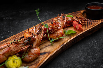 Grilled shrimps, on a wooden board, with sauce, on a dark background