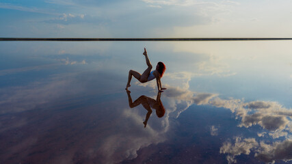 flexible slender girl gymnast performs dance posing in the reflection of the sky. salt lake, dancer against a dramatic sky with clouds
