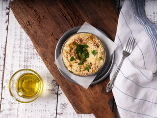 Hummus and olive oil with fork on a metal plate on a wood cutting board on wooden background
