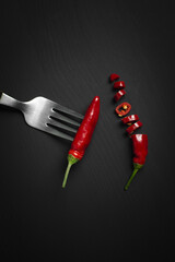sliced hot chili pepper whit fork on black background