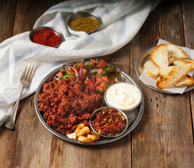 mashed sausage with mezes and toasted bread and a fork on a metal plate on wooden background

