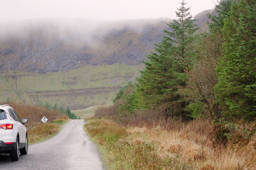 Small car parked off road by a forest. Mountains in the background. Gleniff horseshoe drive, county Sligo, Ireland. Travel concept