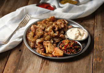 kokorec with mezes and a fork and spices on a metal plate on wooden background
