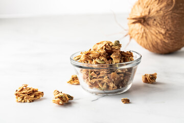 Close up of a small glass bowl filled with coconut clusters against a light background.