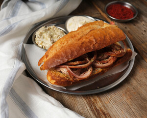 Kokorec sandwich with red crushed pepper and hummus on a metal plate on wooden background
