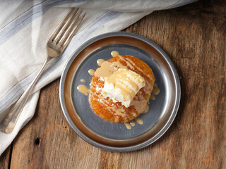 bread pudding with cream with a fork on a metal plate on wooden background