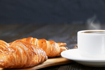 A cup of hot coffee and croissants on a wooden background. Breakfast with coffee and fresh pastry. Copy space. Fresh cake and pastry