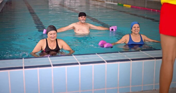 Coach and senior group water aerobics class with dumbbells