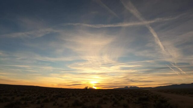 Golden sunset and colorful, dynamic cloudscape over the arid terrain of the Mojave Desert - wide angle time lapse