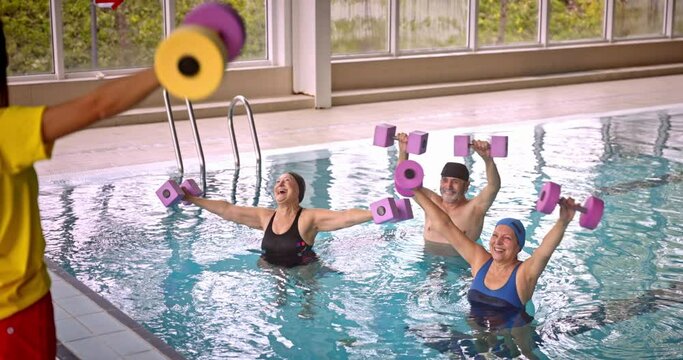 Group of seniors in aerobics class raising dumbbells with instructor