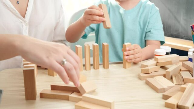 Little toddler boy putting wooden blocks or domino in long line. Concept of children education at home during lockdown and staying at home.Parents playing with children