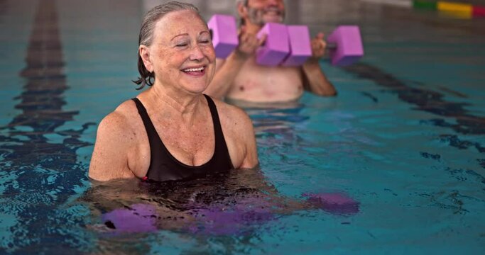 Senior woman exercising with dumbbells in aerobics class in pool