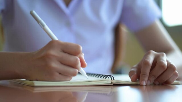 Young lady's hand holding pen writing new appointments information in organizer concept,making notes in personal paper planner at desk, close up view.