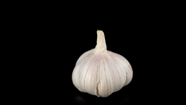 unpeeled garlic bulbs rotates isolated on black background