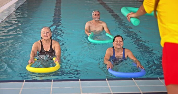 Coach giving pool noodle senior aerobics class in pool
