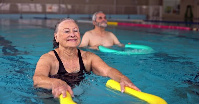 Senior woman exercising with pool noodle during water aerobics class