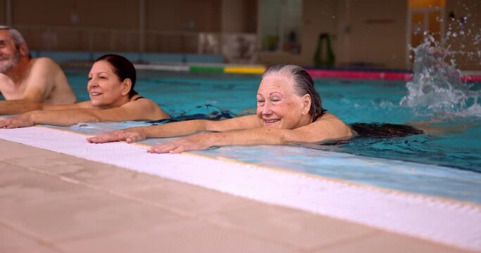 Group of seniors holding poolside splashing feet exercising in pool