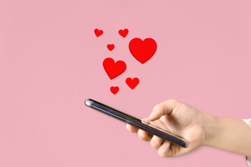 Female hands holding mobile phone with hearts, Love symbol on pink background. Valentine's day concept.