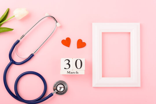 Doctor's Day concept, flat lay top view, equipment medical red heart stethoscope and photo frame on pink background, care patient in hospital with copy space for text