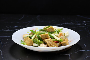 Fried and stirred cutting soft tofu with fresh peeled shrimp, basil, chilly and spring onion serving on the plate. Famous traditional hot and spicy food in Asia restaurant. 