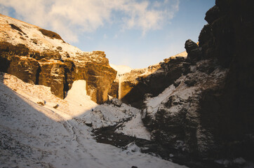 Sun setting in Waterfall Canyon in Iceland during winter with people on the trail to the waterfall. 