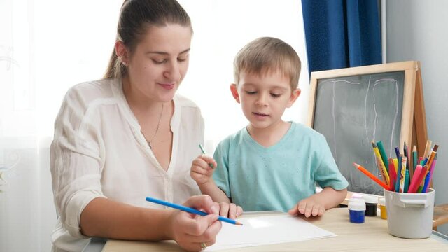 Teacher teaching drawing her little toddler son with colorful pencils at school classroom. Concept of parenting and education at home. Creativity and children art