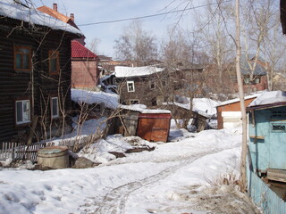 Leaning simple wooden houses and metal garages in the snow in the light of the sun